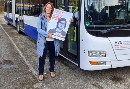 Eine Frau steht mit einem Plakat vor einem Bus.