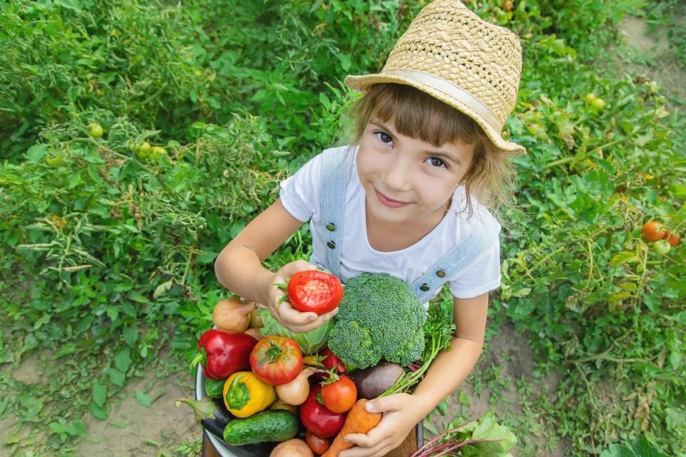 Mädchen mit einer Schale voller Gemüse und einer Tomate in der Hand