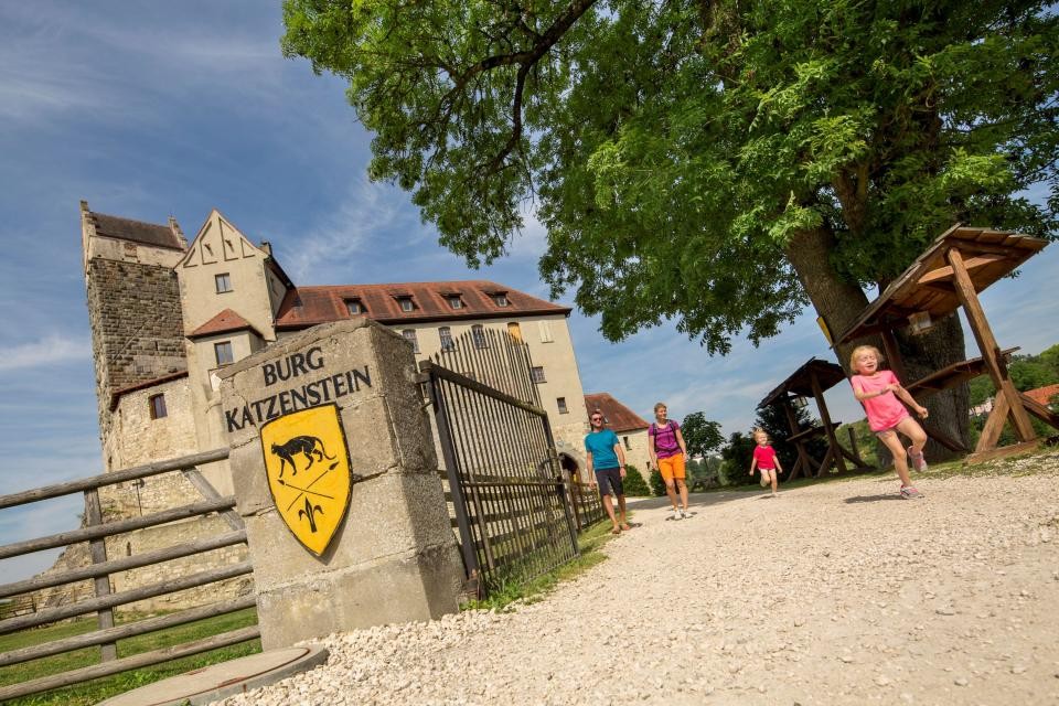 Zwei fröhliche Kinder mit ihren Eltern laufen aus dem Eingang der Burg Katzenstein heraus.